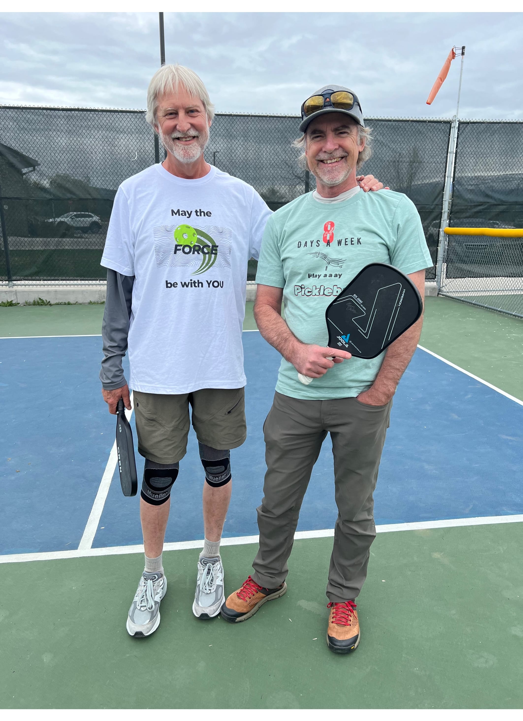 Keven and Stuart posing in two different BestPickleballTees Unisex T-shirts on a Pickleball court