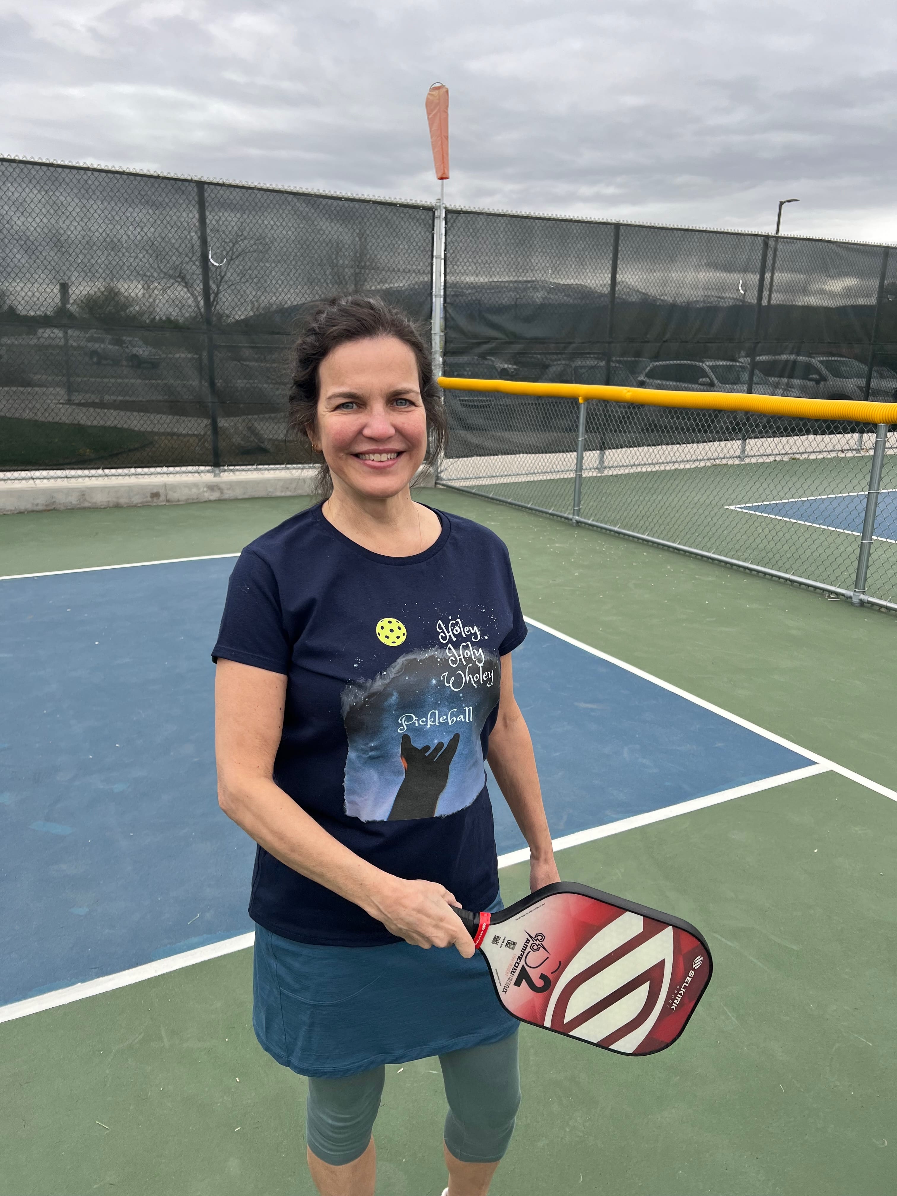 On a Sunday, Lisa posed wearing the Holey, Holy, Wholey Pickleball T-shirt.  A hand reaches to the heavens and a pickleball floats above the words and image