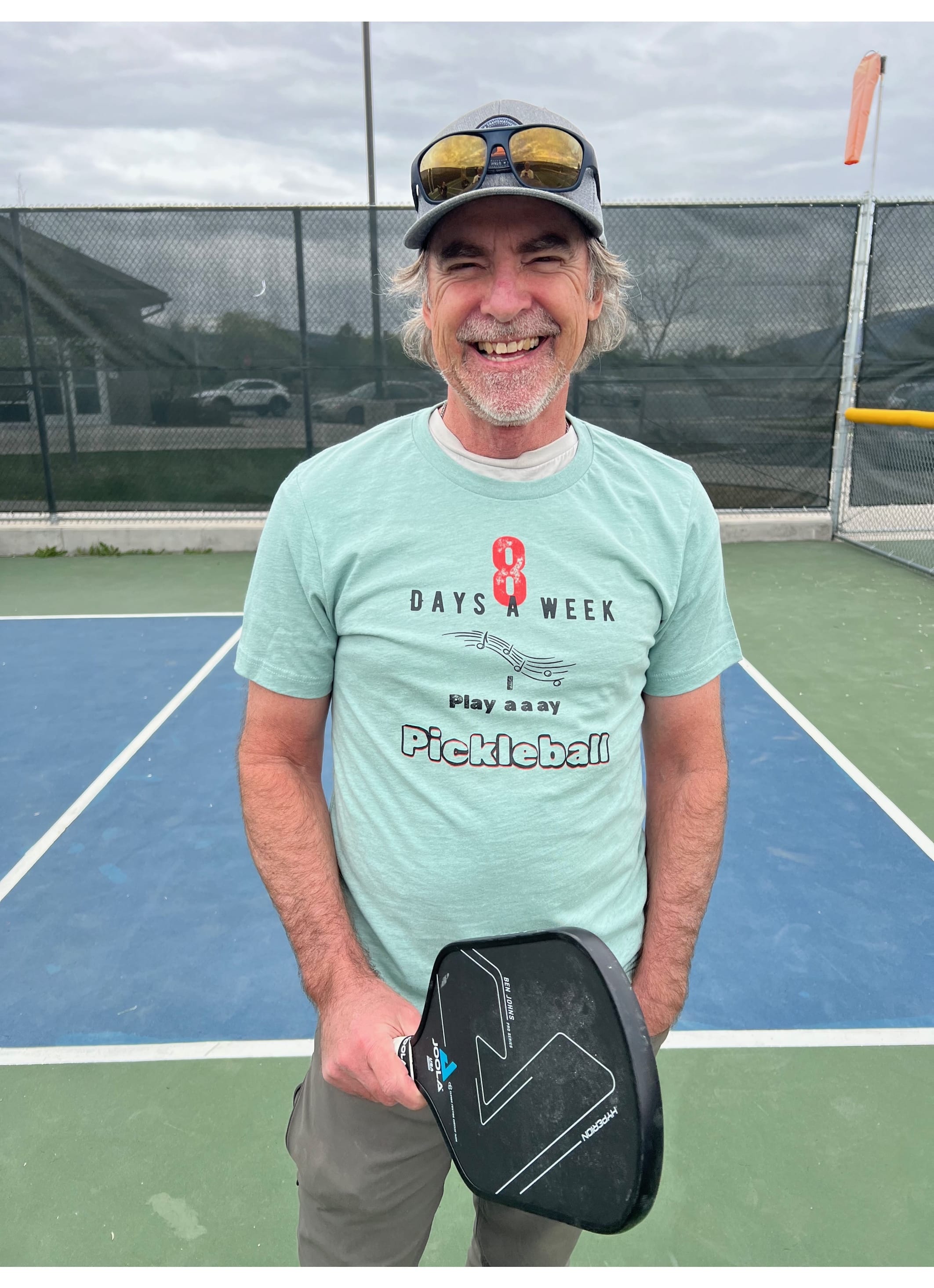 Kevin is wearing an 8 Days a Week I play a a ay Pickleball T-shirt posing in a pickleball court