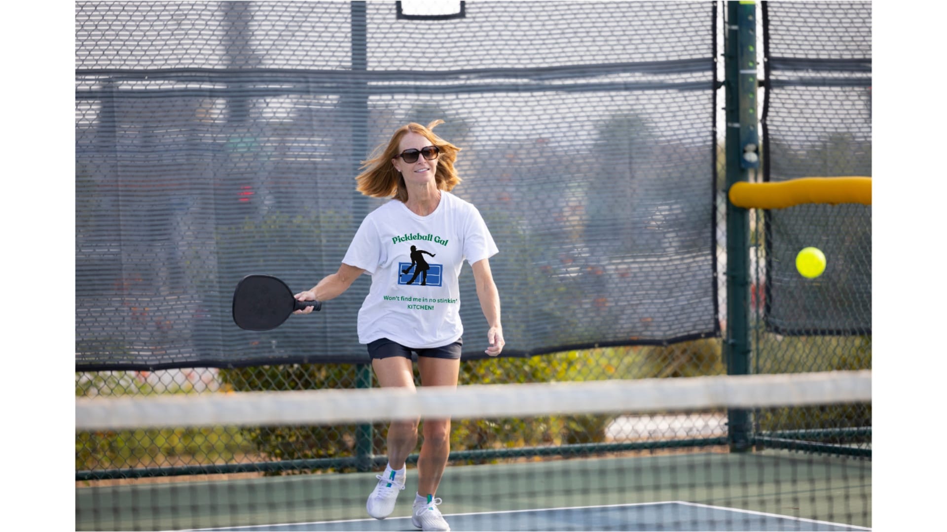 Pickleball T-shirt Image of female figure with paddle standing across a pickleball court with the words: Won't Find Me in No Stinkin Kitchen